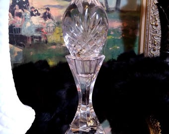 May include: A clear glass bottle stopper with a faceted design. The stopper is on a clear glass base with a faceted design. The stopper is on a black fur surface.
