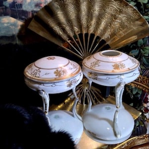 May include: Two white porcelain trinket boxes with gold accents and floral designs. The boxes are on a gold tray with a black fur trim.