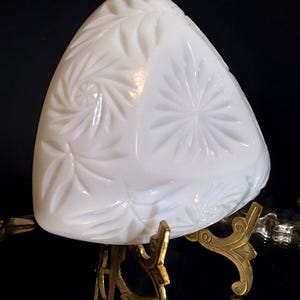 May include: A white, triangular-shaped decorative dish with a floral pattern. The dish is supported by a gold-colored metal stand with ornate detailing. The background is black.