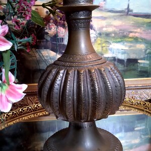 May include: A large, ornate, dark brown metal vase with a wide base and a narrow neck. The vase has a decorative, fluted design and intricate details.