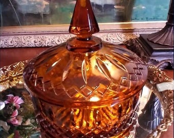 May include: A vintage amber glass candy dish with a domed lid and a diamond pattern. The dish is sitting on a gold-colored tray with a floral design.