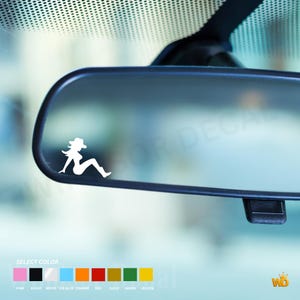 May include: A white vinyl decal featuring the silhouette of a person wearing a cowboy hat and boots, shown in a seated pose. The decal is applied to the surface of a vehicle rearview mirror, with a colour selection chart visible at the bottom.