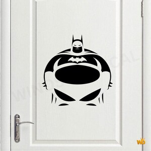 May include: A black vinyl decal featuring a stylised, round-bodied Batman character with a prominent bat emblem on the chest, pointed ears on the cowl, and a wide, circular torso design, applied to the centre of a white panelled door.