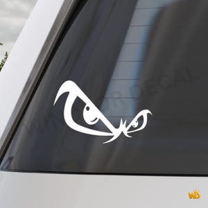 Peut inclure: Autocollant en vinyle blanc représentant des yeux stylisés et en colère, appliqué sur une vitre de voiture. Le design présente des lignes nettes et angulaires et une expression menaçante. L'autocollant est un accessoire populaire pour les véhicules.