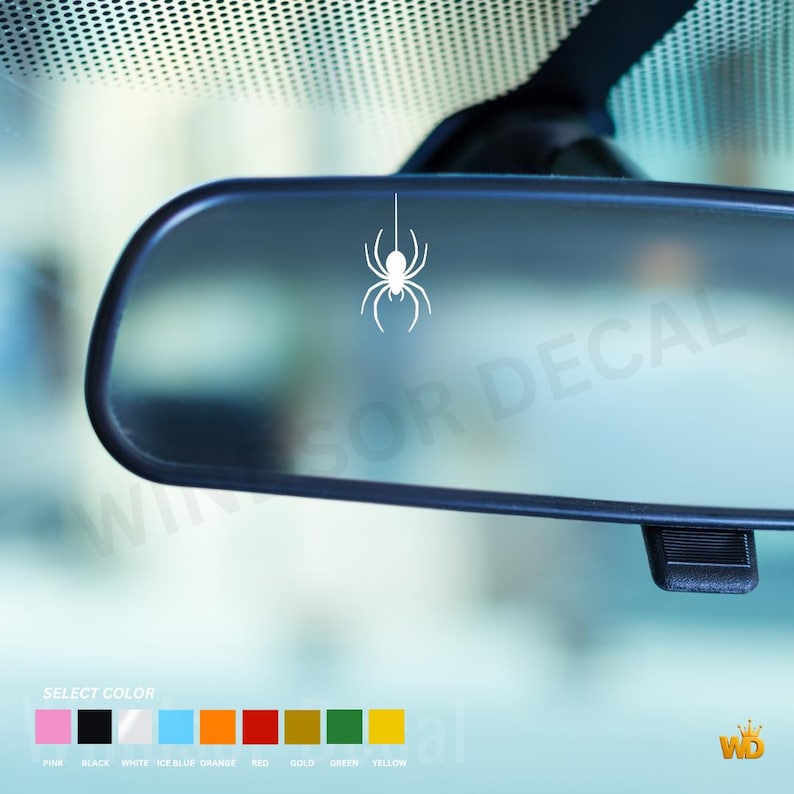 Puede incluir: Un adhesivo de ara&ntilde;a blanco aplicado en el centro de un espejo retrovisor de coche. Debajo del espejo, una tabla de selecci&oacute;n de color muestra opciones que incluyen rosa, negro, blanco, azul hielo, naranja, rojo, oro, verde y amarillo.
