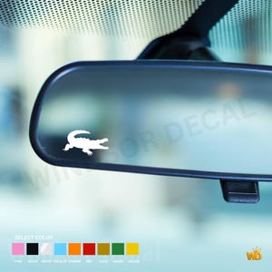 Può includere: Un adesivo in vinile bianco con la sagoma di un coccodrillo applicato su uno specchietto retrovisore per auto. Sotto lo specchietto, una tabella di selezione dei colori mostra opzioni tra cui quadrati rosa, neri, bianchi, blu ghiaccio, arancioni, rossi, oro, verdi e gialli.