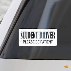 Peut inclure: Autocollant rectangulaire blanc avec le texte "STUDENT DRIVER PLEASE BE PATIENT" en noir et gris. L'autocollant est apposé sur la vitre arrière d'un véhicule blanc.