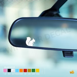 Peut inclure: Un autocollant silhouette d'écureuil blanc appliqué sur un rétroviseur de véhicule. Sous le rétroviseur, un nuancier affiche neuf échantillons de couleurs étiquetés rose, noir, blanc, bleu glace, orange, rouge, or, vert et jaune.