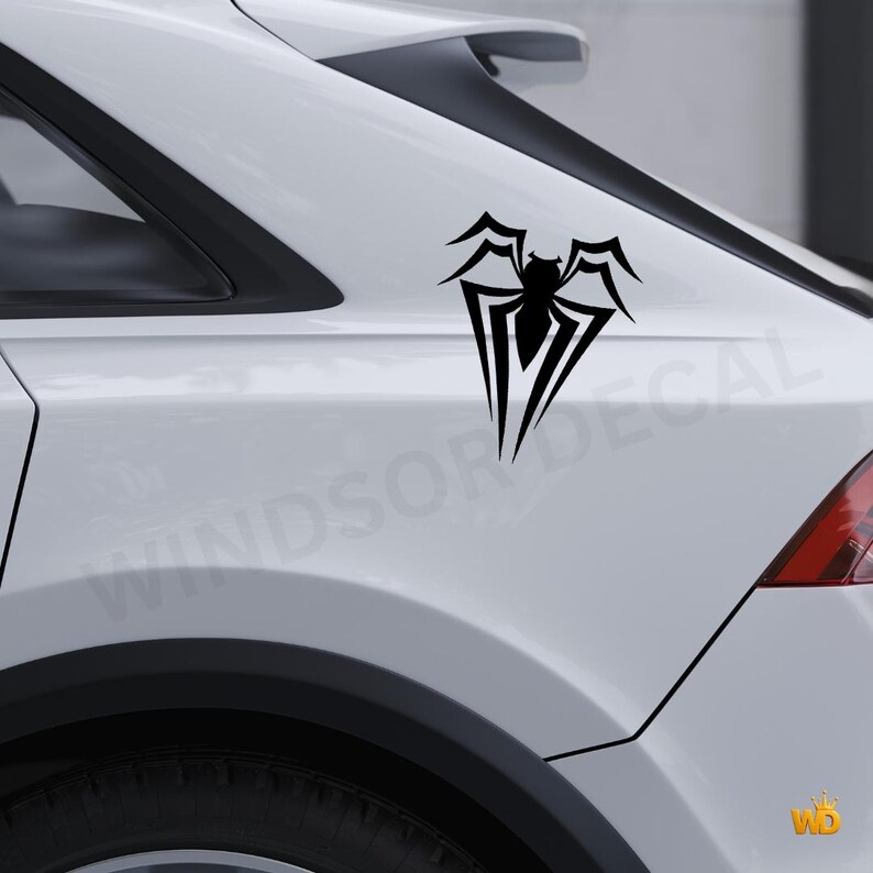 May include: Black spider emblem car decal. The decal is a stylized spider design with sharp lines and a symmetrical shape. The decal is applied to the white body of a car. The text "WINDSOR DECAL" is visible in the background.