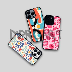 May include: Three different phone cases with colorful abstract designs. The first case has a blue, orange, and black abstract design. The second case has a pink and red design with lips. The third case has a white background with blue, red, and orange abstract shapes.