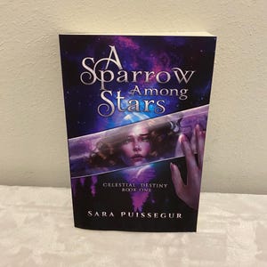 May include: A book cover with a purple, blue, and white background. The title is "A Sparrow Among Stars" with the words "Celestial Destiny Book One" and "Sara Puissegur" below. The cover features a woman with long brown hair looking out of a window.
