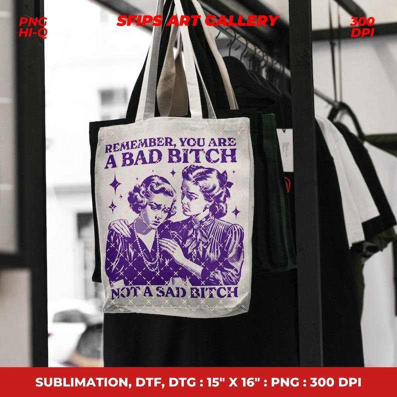 May include: A white tote bag with a purple graphic of two women and the text "REMEMBER, YOU ARE A BAD BITCH NOT A SAD BITCH." The bag is 15" x 16" and has black handles. The bag is hanging on a rack with other clothing.