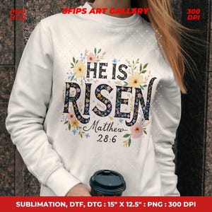 May include: White sweatshirt with the text "HE IS RISEN" in a floral design. The text "Matthew 28:6" is below the main text. The sweatshirt has a crew neck and long sleeves. The image also includes the text "SFIPS ART GALLERY".