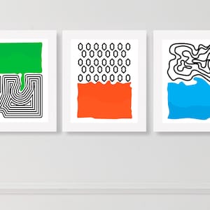 May include: Three abstract art prints with white frames. The first print features a green shape with a black and white maze pattern underneath. The second print features a black and white honeycomb pattern with an orange shape underneath. The third print features a blue shape with a black maze pattern above.