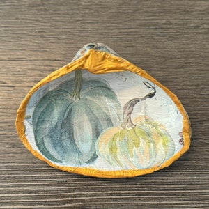 May include: A decorative ceramic dish with a gold rim and a painted design of two pumpkins. The pumpkins are green and white with a watercolour effect.