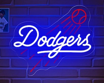 May include: A blue and red neon sign with the word "Dodgers" in white lettering. The sign is lit up and hanging on a brick wall. There are baseball pictures on the wall behind the sign.
