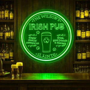May include: A neon green sign for "The Wilson's Irish Pub" with text and a pint of beer with a shamrock. The sign includes the words "singin' dancin' carryin'on", "drink, good friends & blarney", and "Sláinte". Two glasses of beer sit on the bar.