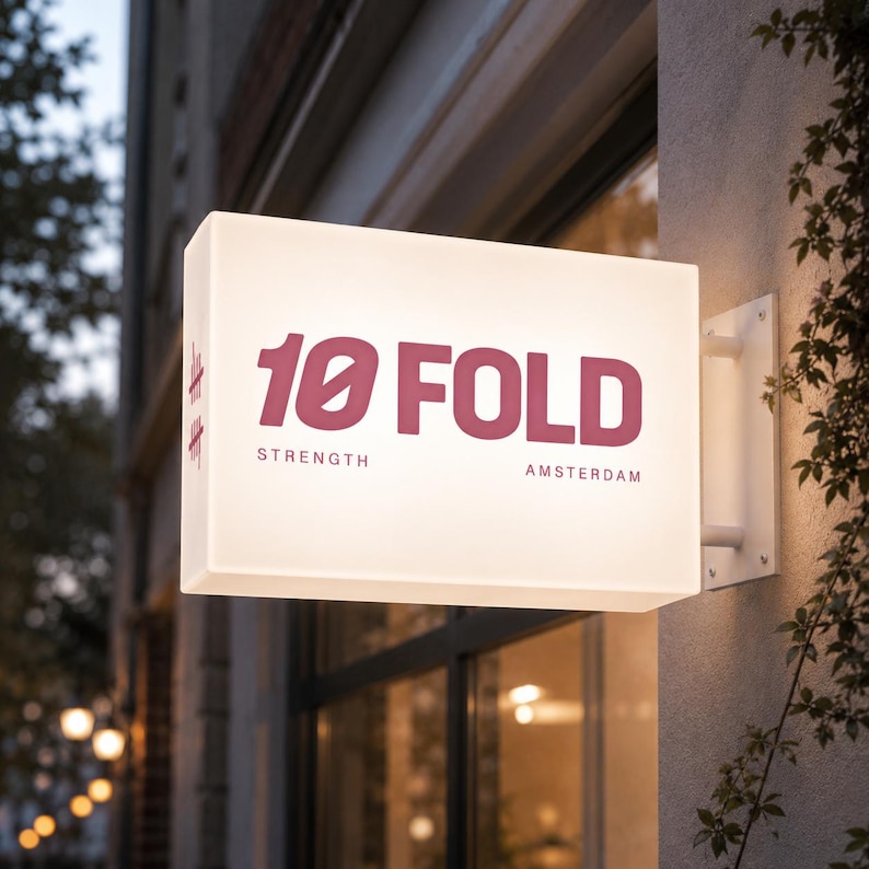 K&ouml;nnte beinhalten: Ein rechteckiges, beleuchtetes Wand-Schild mit einer wei&szlig;en, durchscheinenden Oberfl&auml;che. Das Schild zeigt den dunkelrosa Schriftzug 10 FOLD, wobei das Wort STRENGTH links und AMSTERDAM rechts darunter in kleinerer Schriftart angebracht sind.