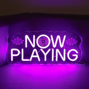 May include: A white neon sign with the words "NOW PLAYING" and a stylised record icon. The sign is illuminated with a purple glow.