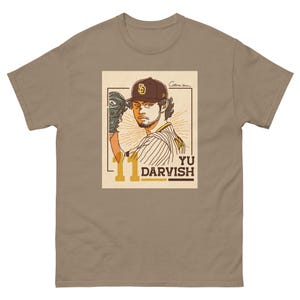 Peut inclure: Un t-shirt beige avec une illustration vintage d'un joueur de baseball portant un maillot des Padres de San Diego. Le joueur tient un gant de baseball et est en position de lancer. Le texte "Yu Darvish" et le numéro "11" sont imprimés sur le t-shirt.