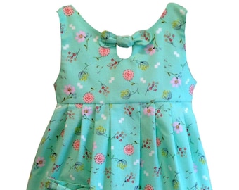 May include: A sleeveless, mint green dress with a floral print and a bow at the back. The dress has a pocket on the front with a bow.
