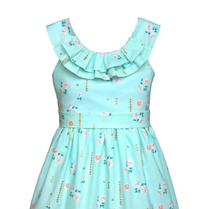 Op de afbeelding: Lichtblauwe jurk met bloemenpatroon. De jurk heeft een gerimpelde halslijn en een getailleerde taille. De stof is versierd met roze rozen, gouden driehoeken en verticale gouden lijnen. De jurk is voor kinderen.