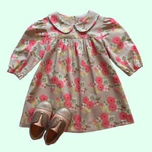 Könnte beinhalten: Ein beiges Kleid mit rosafarbenem Blumendruck und einem weißen Peter-Pan-Kragen. Das Kleid hat lange Ärmel und einen gerafften Rock. Das Kleid wird mit braunen und goldenen Schuhen kombiniert.