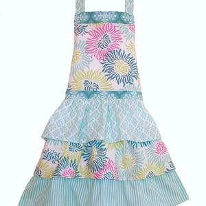 May include: A turquoise blue and white floral print apron with a ruffled skirt. The apron has three tiers of ruffles and a wide, floral print waistband.
