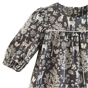 Puede incluir: Un vestido de manga larga de color gris oscuro con estampado floral y animal blanco. El estampado presenta ciervos, pájaros, ardillas y setas.