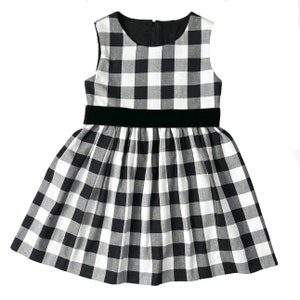 Puede incluir: Un vestido sin mangas de cuadros vichy blanco y negro con un cintur&oacute;n de terciopelo negro.