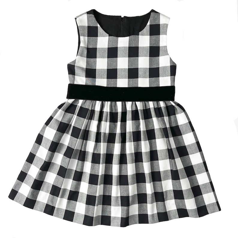 Puede incluir: Un vestido sin mangas de cuadros vichy blanco y negro con un cintur&oacute;n de terciopelo negro.