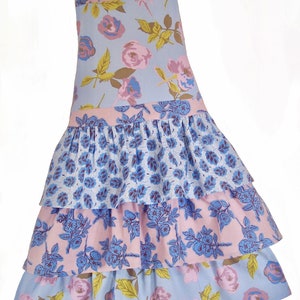 May include: A blue and pink floral print apron with a ruffled skirt. The apron has three tiers of ruffles and features a variety of floral patterns.
