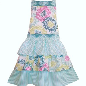 May include: A turquoise and white tiered apron with a floral print. The apron has a wide ruffle at the bottom and a smaller ruffle at the waist.