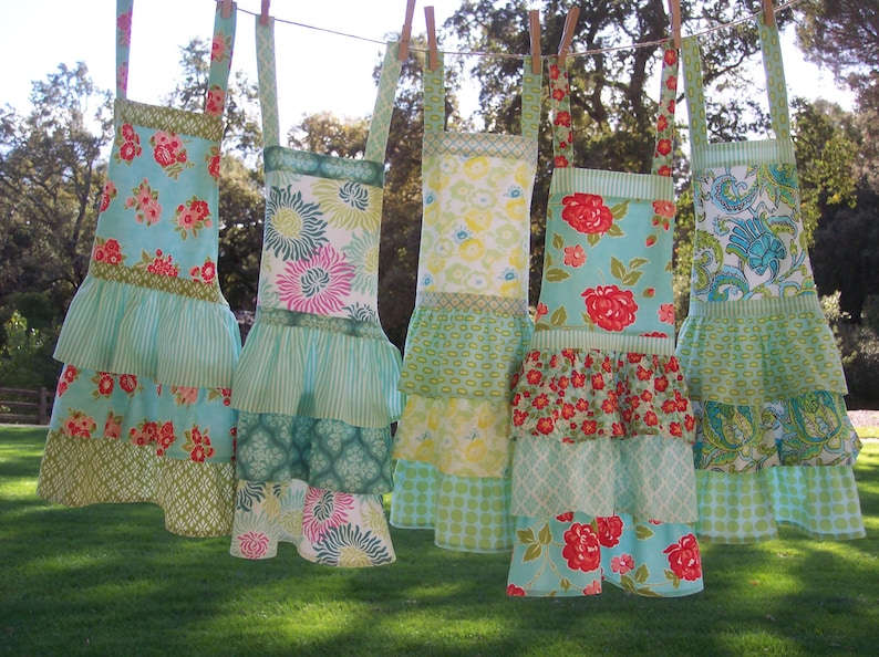 May include: Five colorful ruffled aprons with floral patterns. The aprons are hanging on a clothesline outdoors.