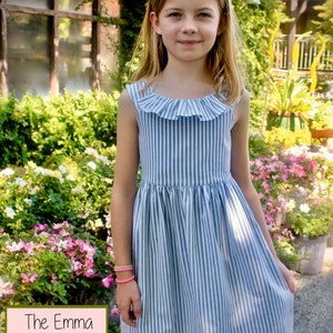 May include: A blue and white striped dress with a ruffled neckline. The dress is sleeveless and has a flared skirt. The text "The Emma Rose Dress" is in a pink box in the lower left corner. The girl is wearing a pink bracelet.