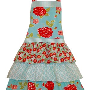 May include: A turquoise blue apron with a tiered ruffle skirt. The apron has a floral print with red roses and smaller white flowers. The straps are also floral print.