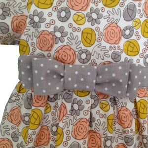 May include: A white dress with a gray polka dot bow and a floral print featuring peach, yellow, and gray flowers.