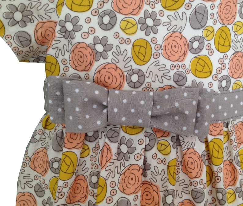 May include: A white dress with a gray polka dot bow and a floral print featuring peach, yellow, and gray flowers.