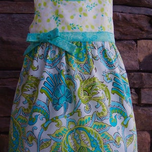 May include: A white dress with a green and blue floral pattern. The dress has a green and blue ribbon tied at the waist.