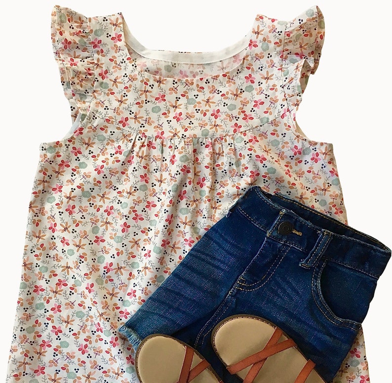 May include: A white sleeveless blouse with a floral print and ruffled sleeves. The blouse is paired with blue denim shorts and brown sandals.