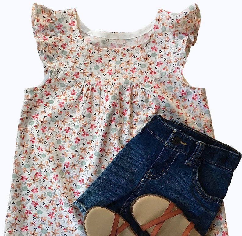 May include: A white sleeveless top with a floral print and ruffled sleeves. The top is paired with blue denim shorts and brown sandals.