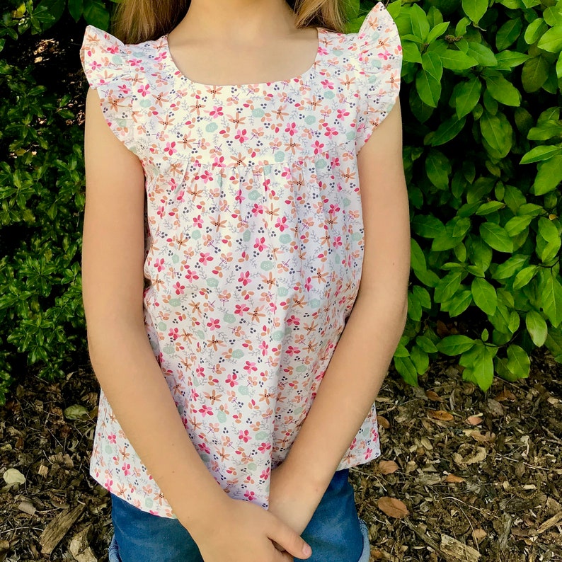 May include: A white sleeveless blouse with a floral print and ruffled trim. The blouse has a scoop neck and a gathered bodice.