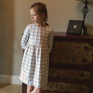 Puede incluir: Una ni&ntilde;a peque&ntilde;a con un vestido blanco y negro de cuadros vichy con falda fruncida.
