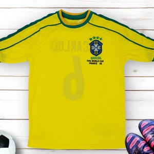 May include: Yellow football shirt with green trim and the number 9 on the front. The shirt has the Brazilian national team logo and the text "BRASIL FIFA WORLD CUP FRANCE '98".