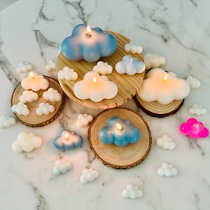 May include: A collection of cloud-shaped candles in white and blue, with some candles on wooden coasters. The candles are arranged on a white marble surface.