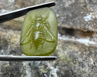 May include: A green glass cameo with a detailed carving of a bee. The bee is in a raised relief and has visible wings, legs, and antennae.