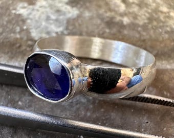 May include: A silver ring with a deep blue oval gemstone set in a bezel setting. The ring has a hammered finish and a wide band.