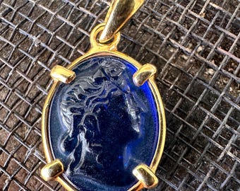 May include: A gold pendant with a blue glass cameo featuring a profile of a woman's face.