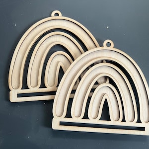 May include: Two unfinished wooden rainbow ornaments with a layered design. Each rainbow has four layers and a flat base.