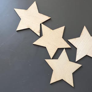 Peut inclure: Quatre étoiles en bois non finies de différentes tailles sur un fond gris.